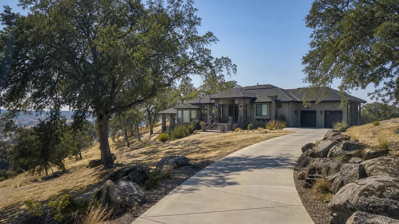 Hillside foothill home with a sloped concrete driveway, granite boulders, oaks and dry golden grass