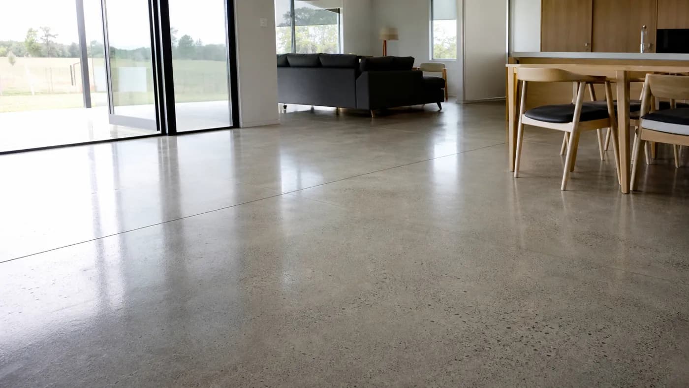 Interior of a modern home with a light gray polished concrete floor reflecting window light, faint aggregate and saw-cut joint lines