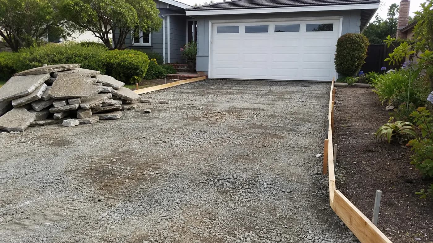 Old driveway removed, with broken slabs stacked, gravel base exposed and new wood forms set for the replacement pour
